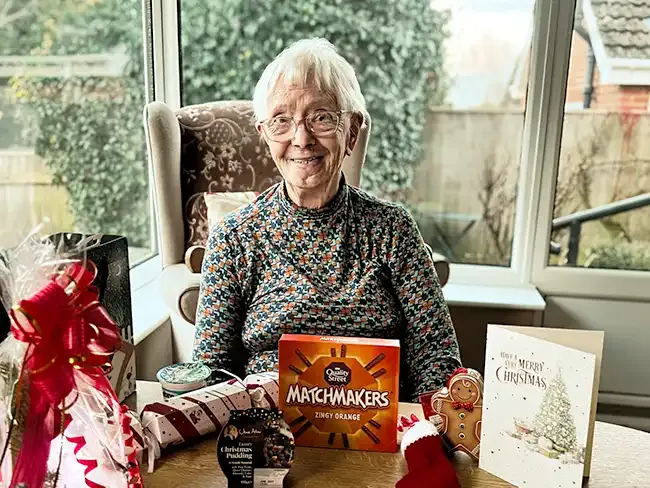 Client smiling while sitting at a table with Christmas treats including Matchmakers, a pudding, a cracker, and a festive gift basket.