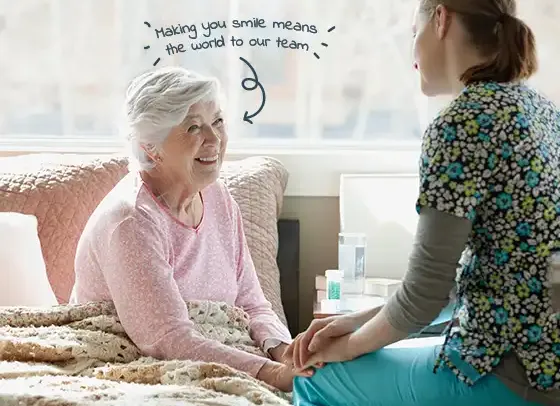 Elderly woman smiling while receiving compassionate home care support from a caregiver, showing warmth and reassurance in a comfortable home setting.