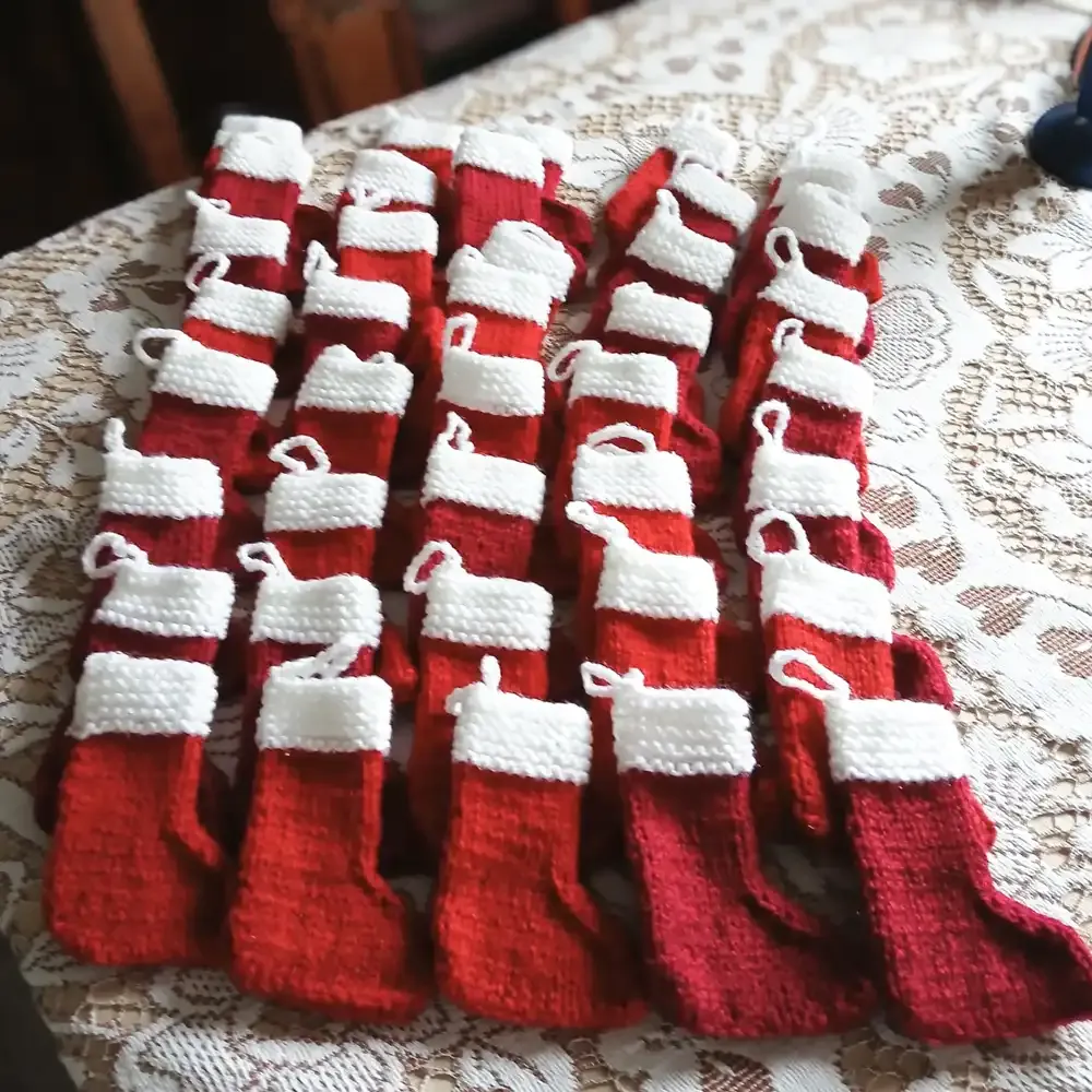 Hand-knitted mini red-and-white Christmas stockings laid out on a table, made to add a personal touch to client gift baskets.
