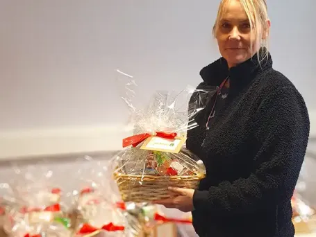 Team member holding a wrapped Christmas gift basket with a personalised tag, with multiple client gift baskets prepared in the background at The Great Care Company.