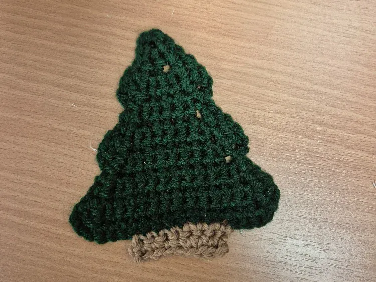 Handmade crocheted Christmas tree decoration in dark green yarn on a wooden tabletop.