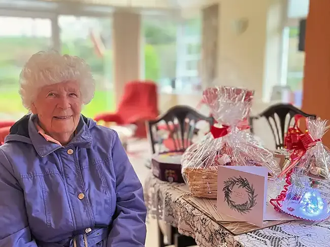 Client sitting at a decorated table with Christmas gift baskets, a festive card, and a glowing ornament.