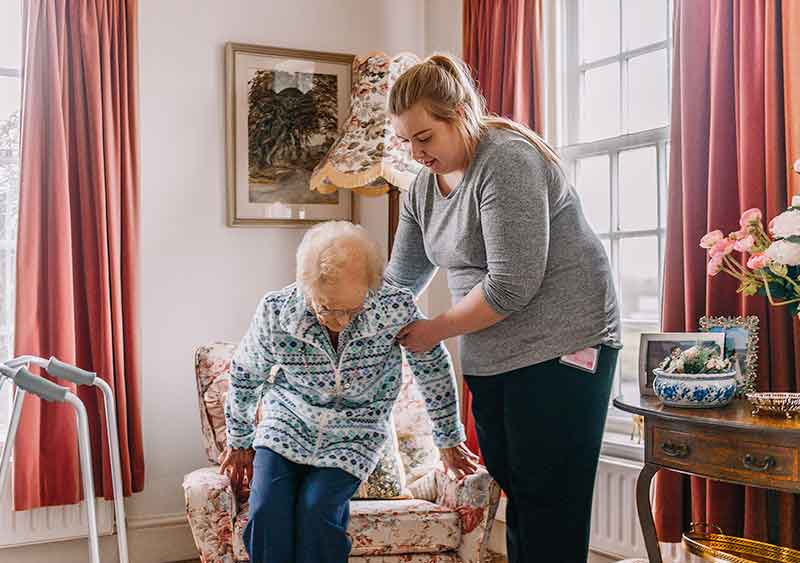 health carer helping Rosemary into her chair before she tells her health care story