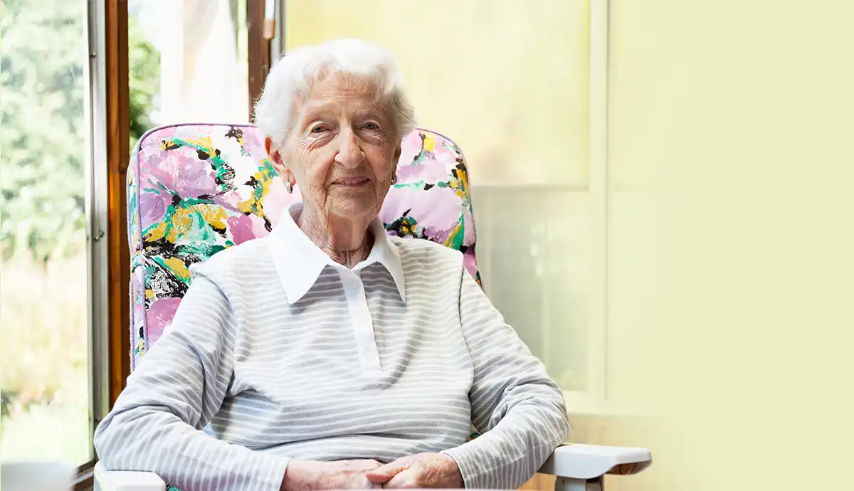Smiling elderly woman sitting comfortably at home with natural light, representing compassionate elderly care at home.