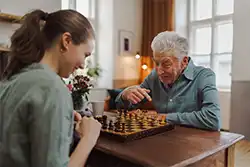 Senior man playing chess with a caregiver to support mental stimulation and independence.