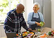A carer assisting an older person with preparing fresh vegetables in the kitchen, showing preventative care at home that supports nutrition and independence.