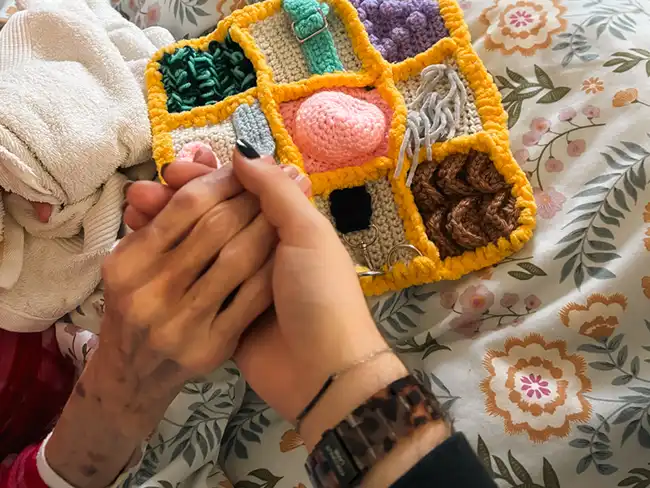 Carer holding woman’s hand while the dementia fidget blanket rests beside them.