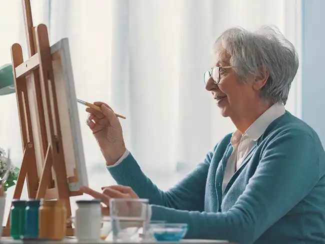 woman painting at an easel, illustrating Christmas gift ideas for older loved ones who enjoy creative hobbies.