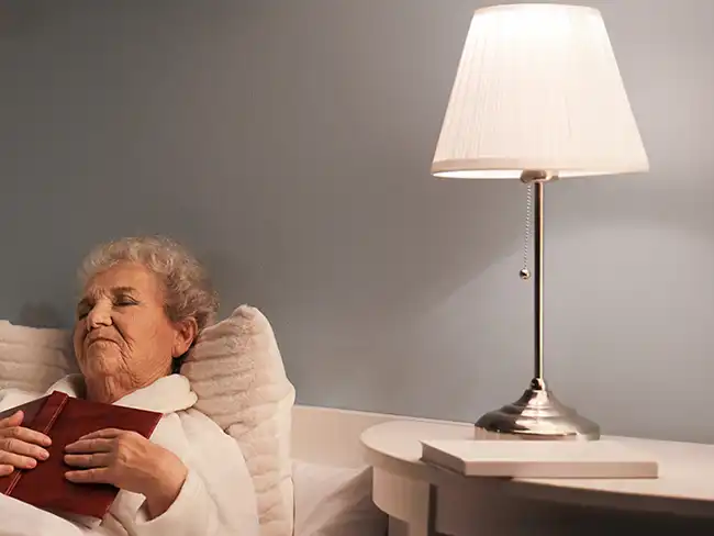 woman resting in bed with a warm bedside lamp, highlighting Christmas gift ideas for older loved ones that support comfort and relaxation.