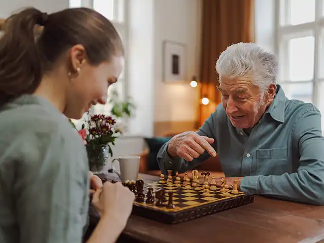 man enjoying a game of chess with a younger woman, representing Christmas gift ideas for older loved ones that encourage quality time and mental stimulation.