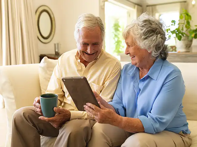couple smiling while using a tablet, highlighting Christmas gift ideas for older loved ones like digital photo frames, video calls and tech gifts.