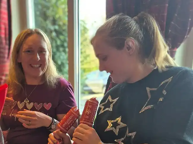 Two women laughing and pulling Christmas crackers during a team festive meal.