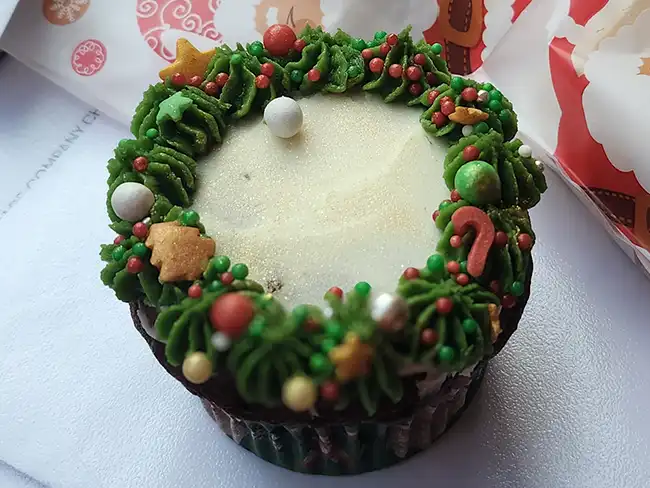 A decorated Christmas cupcake topped with green icing, red and gold sprinkles, and festive decorations.