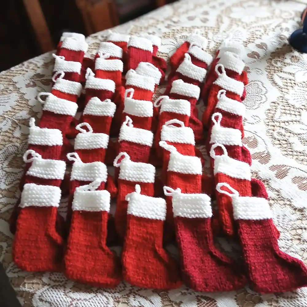 Hand-knitted mini red-and-white Christmas stockings laid out on a table, made to add a personal touch to client gift baskets.