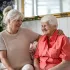 Smiling elderly woman sitting on a sofa with her adult daughter, sharing a warm moment at home — representing compassionate preventative care and family support.