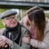 Smiling elderly man with walking stick talking with a young female carer outdoors, showing companionship and good preventative home care.