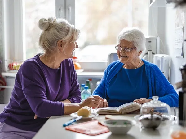 Carer and client with dementia sitting together and laughing, enjoying a moment of connection and joy, demonstrating the importance of companionship in dementia care.