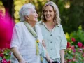 Smiling elderly woman walking with her home carer in a garden, representing the comfort, companionship, and independence offered by home care services in the UK.