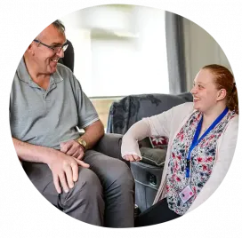 A home care assistant chatting and smiling with an older gentleman while providing companionship in his home.