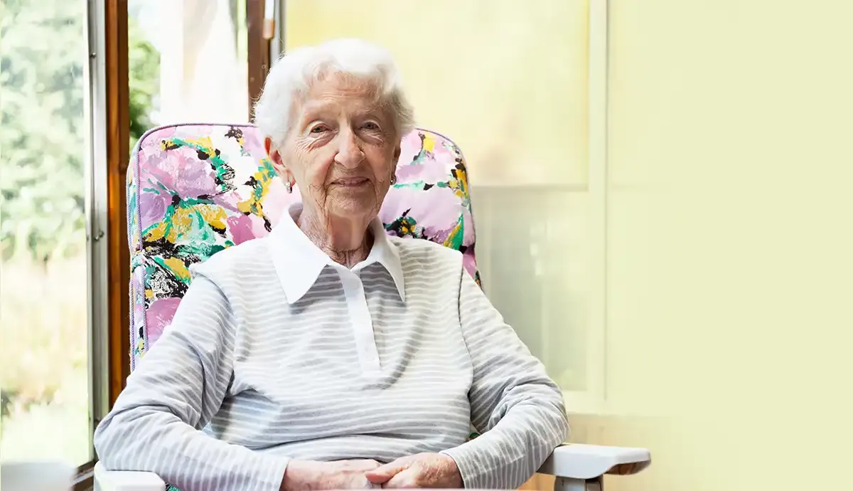 Smiling elderly woman sitting comfortably at home with natural light, representing compassionate elderly care at home.