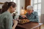Senior man playing chess with a caregiver to support mental stimulation and independence.