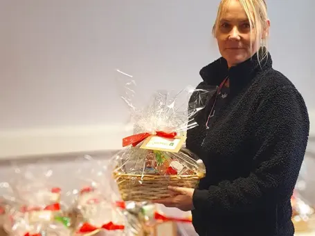 Team member holding a wrapped Christmas gift basket with a personalised tag, with multiple client gift baskets prepared in the background at The Great Care Company.