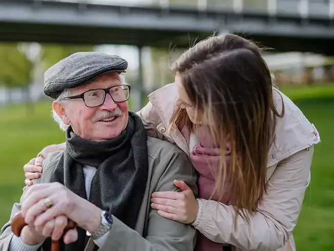 Smiling elderly man with walking stick talking with a young female carer outdoors, showing companionship and good preventative home care.